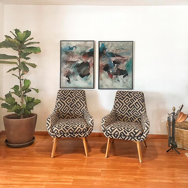 La réception de l'hôtel est décorée de deux beaux fauteuils à motifs géométriques de couleur crème et noire, de deux tableaux accrochés au mur derrière eux et d'une grande plante sur un côté.